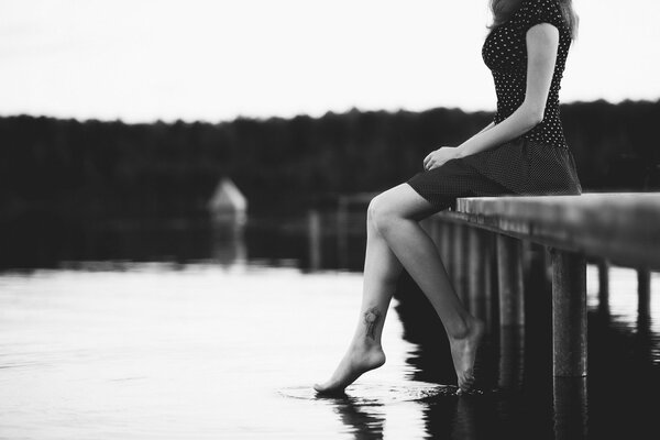 La chica que Mira pensativamente en el agua sobre un fondo blanco y negro