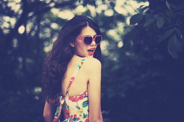 Slender brunette in pink glasses, among the trees, posing for a photo