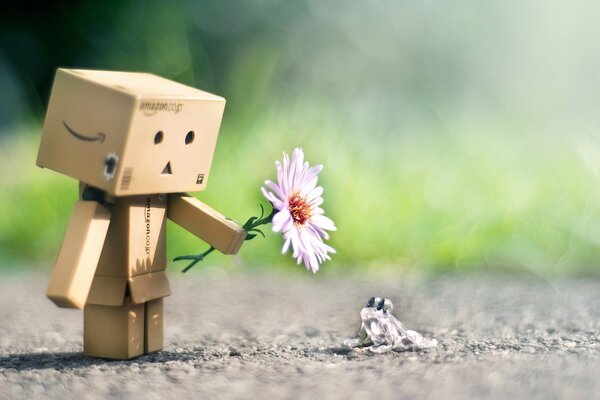 Robot de cartón le da una flor a una rana de vidrio