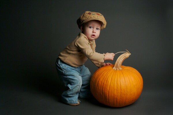 A boy in a cap holds a pumpkin