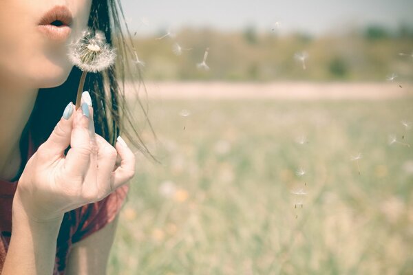 A girl blows a dandelion in the wind