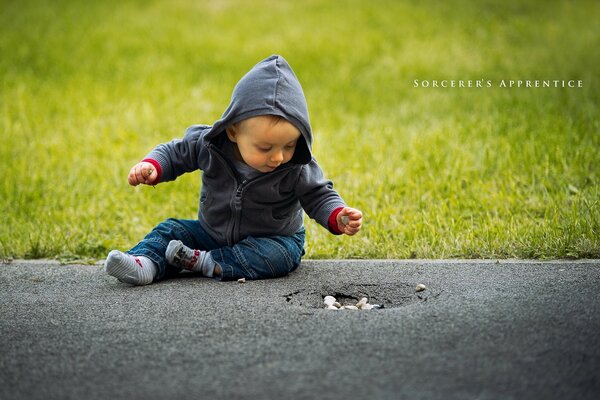 Niño en la calle sentado en el asfalto contra el fondo de la hierba