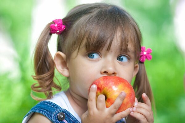 Fille aux yeux bleus et queues de cheval mange une pomme