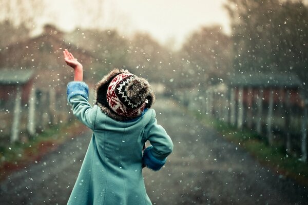 A girl under the snowfall catches snowflakes with her hand