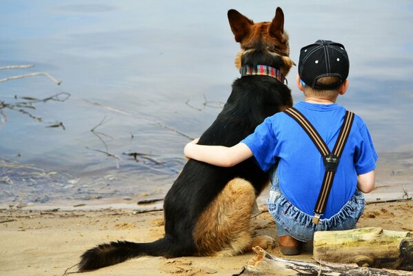 A boy hugs a dog on the shore of a lake