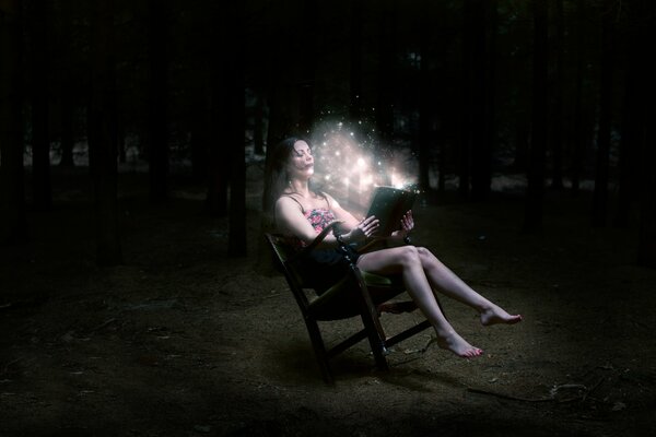 Девушка шатенка сидит в ночном лесу с волшебной книгой