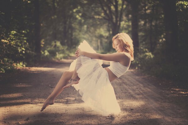 A barefoot girl in a ballet skirt hovering in the air against the background of a forest road