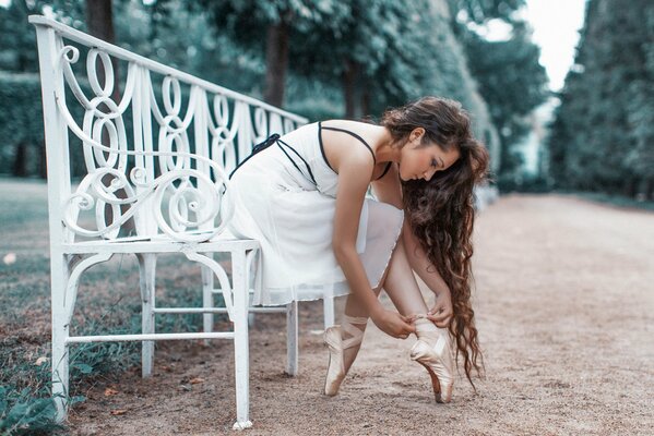 Ragazza che veste le scarpe da punta su una panchina bianca nel parco