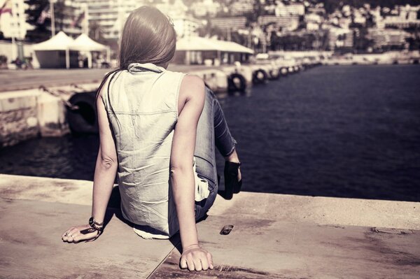 The girl is sitting at the pier in the city