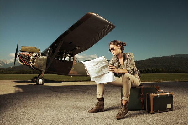 Una chica con un mapa en sus manos, sentada en una maleta al lado de un avión