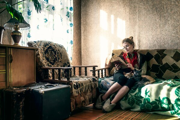 La jeune fille lit un livre assis sur le canapé