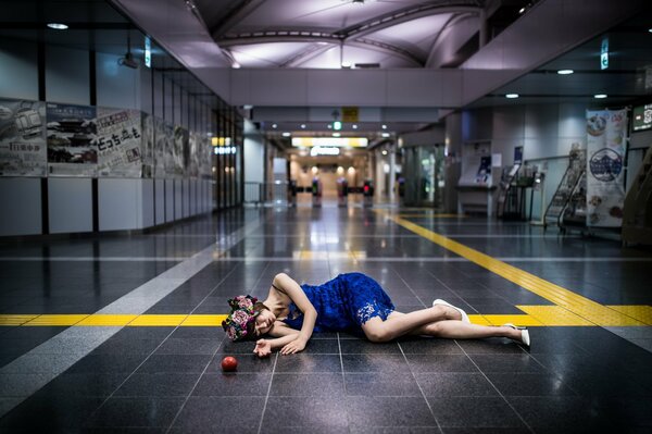 A girl lying in a blue dress on the floor with an apple