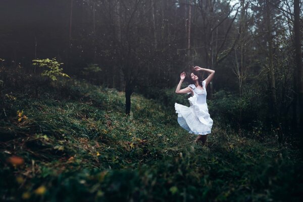 Chica en vestido blanco bailando en el bosque