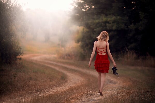 Les jambes nues de la jeune fille dans une robe rouge va sur la route