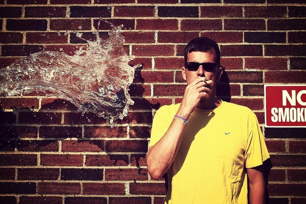 Guy smokes against a brick wall