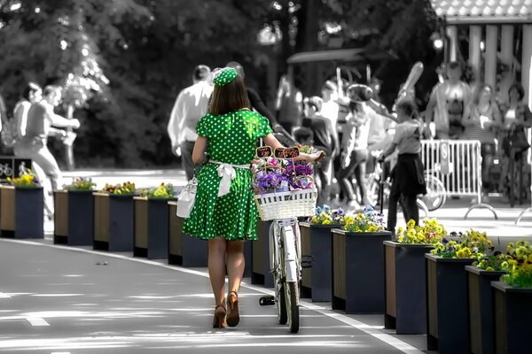 Девушка в зеленом платье ведёт велосипед с цветами