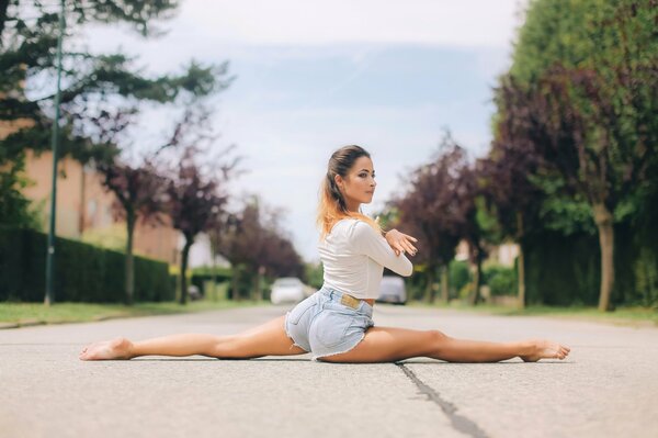 Auf der Straße macht ein Mädchen in Shorts eine Stretching-Schnur