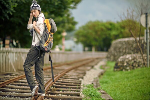 A girl in a hat and with a backpack on the railway