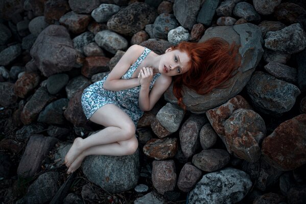 Rothaarige Mädchen mit Sommersprossen liegt auf einem kalten Stein