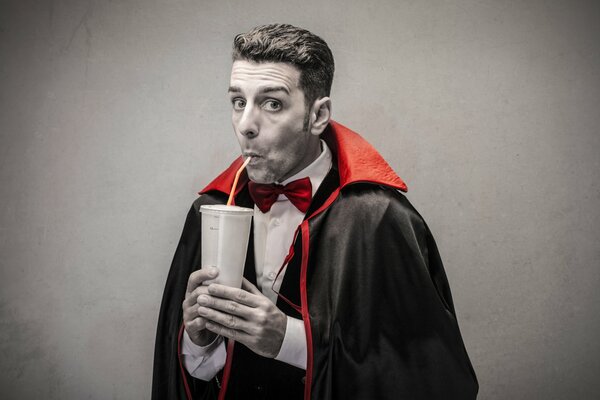 Un uomo vestito da Dracula beve succo da una cannuccia