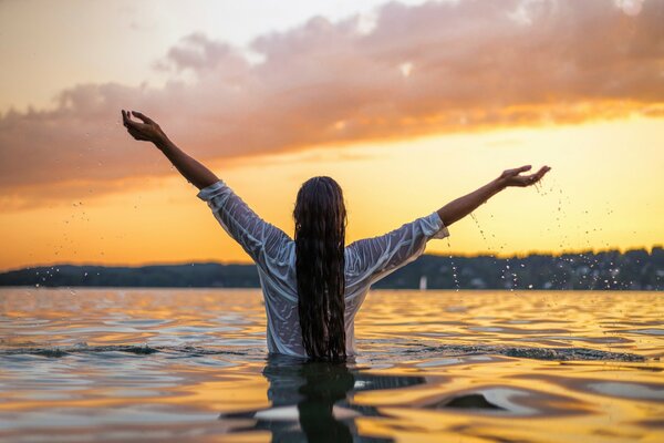 Mädchen steht am Gürtel im Wasser vor dem Hintergrund des Sonnenuntergangs