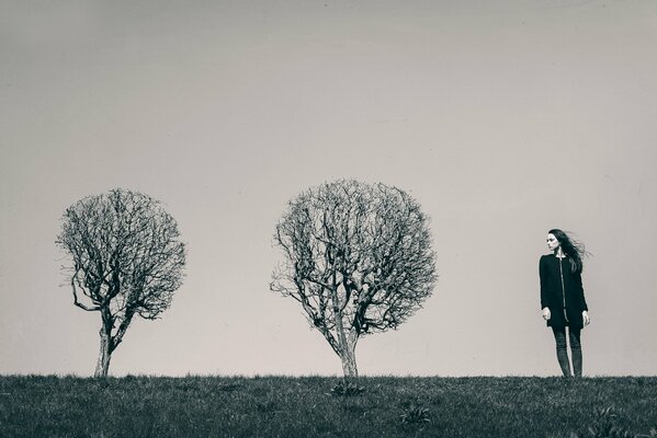 Foto in bianco e nero di una ragazza e due alberi solitari