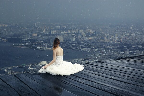 Девушка сидит на крыше высокого здания под дождём