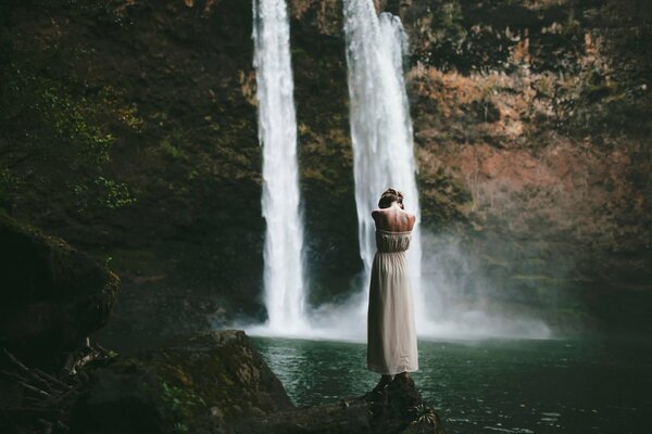 The girl is standing in the water near the waterfall