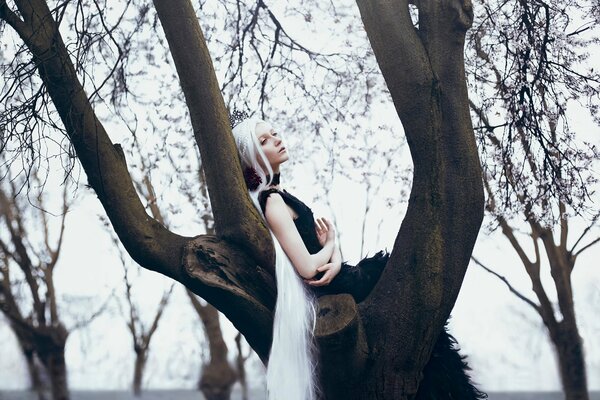 Chica con el pelo largo y blanco y vestido de azufre ena árbol