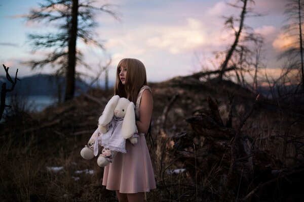 Chica en vestido en el bosque sostiene un juguete-conejito