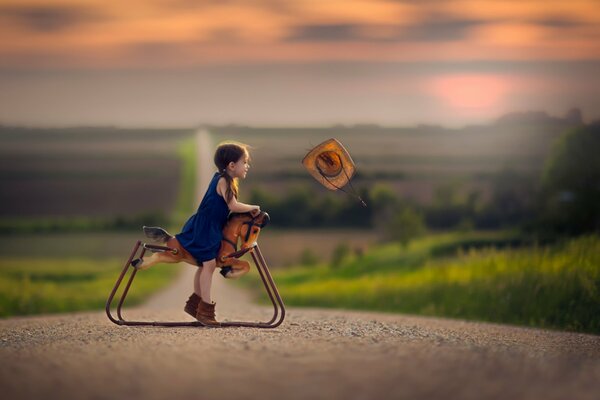 The girl is sitting on a toy horse, the hat was blown by the wind