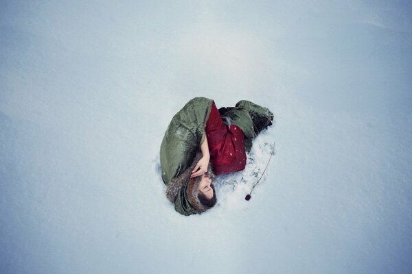 The girl lies on the snow near the red rose