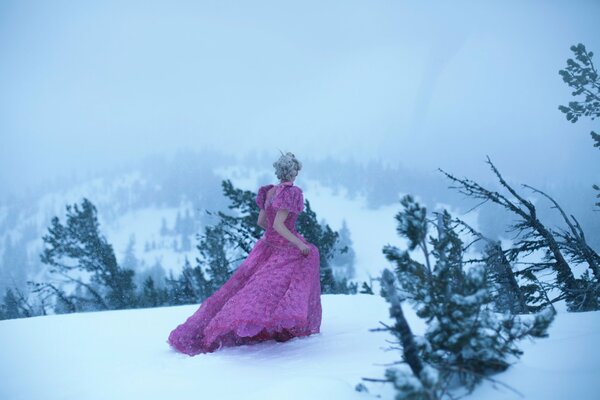 Ragazza in abito lungo rosa che cammina sulla neve