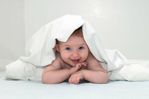 Blue-eyed laughing baby under the blanket