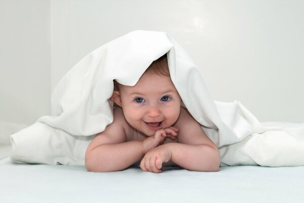 Bebé sonriente de ojos azules debajo de las mantas