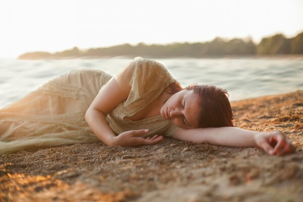 A girl in a long dress is sleeping on the shore