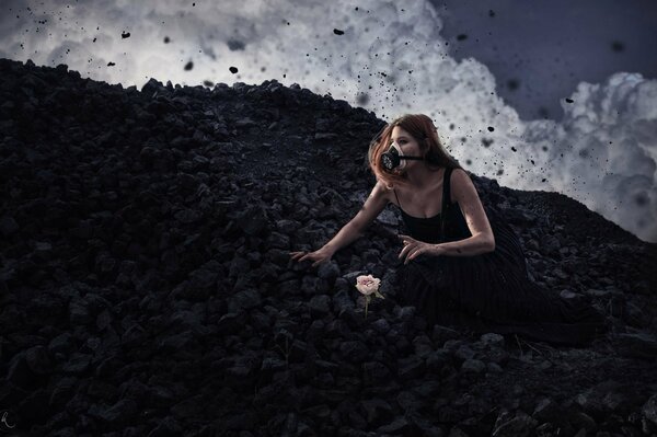 Una chica con un vestido negro y una máscara de gas se sienta junto a una flor