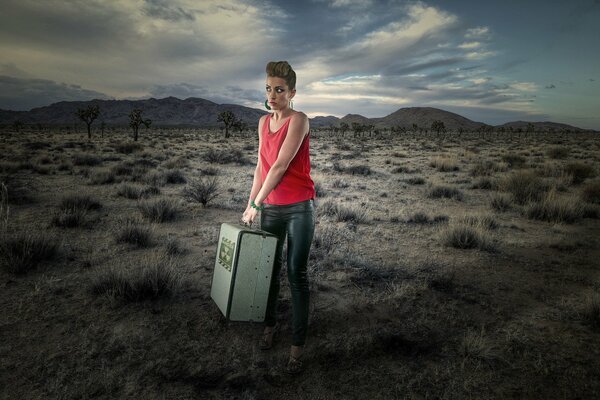 A girl with a suitcase in the desert