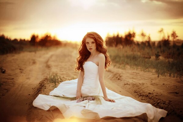 A bride in a wedding dress on a sandy road. There are flowers all around