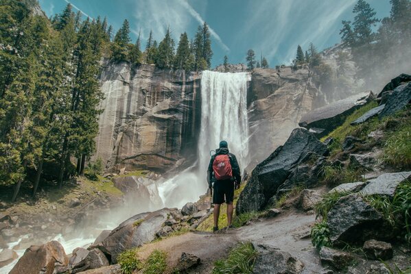 The traveler stands 6a on the rock looking at the waterfall