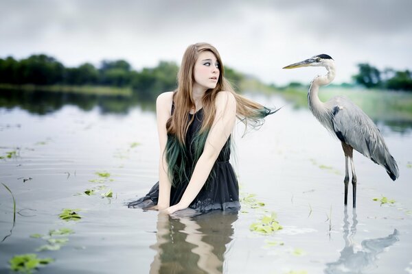 A girl in the water looks at a big bird