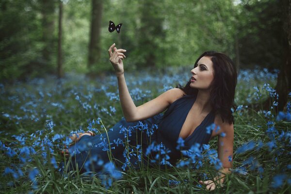 A girl is sitting in blue flowers in the forest