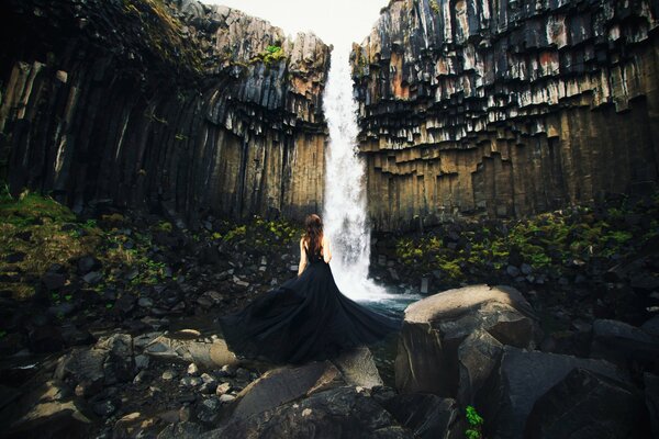 Mädchen im schwarzen Kleid auf dem Hintergrund eines Wasserfalls