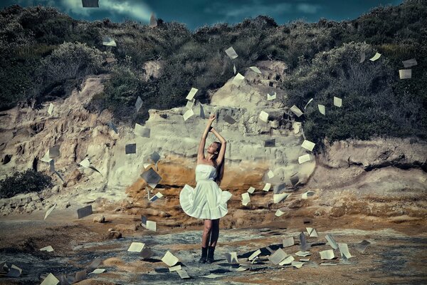 Una chica con un vestido blanco que se desarrolla en el viento, las hojas de los libros vuelan alrededor