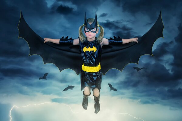 A little girl is flying in a mask and Batman costume