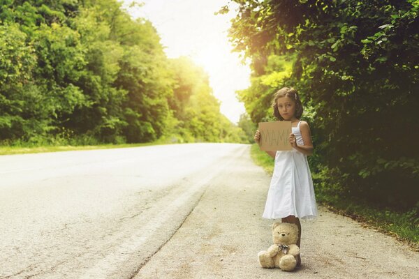 Una niña con un oso de pie en medio de la carretera