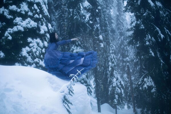 Mädchen im blauen Kleid auf dem Hintergrund der Tannen im Schnee