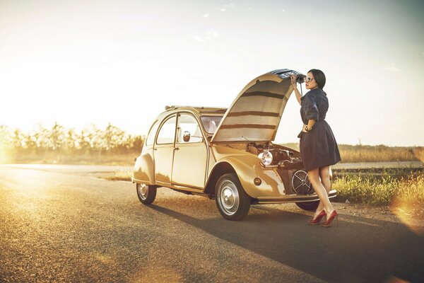 Ragazza sulla strada sbircia sotto il cofano di una Citroen 2cv