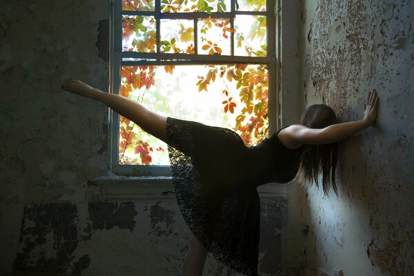 A girl in a ballet pose in a black dress against the wall