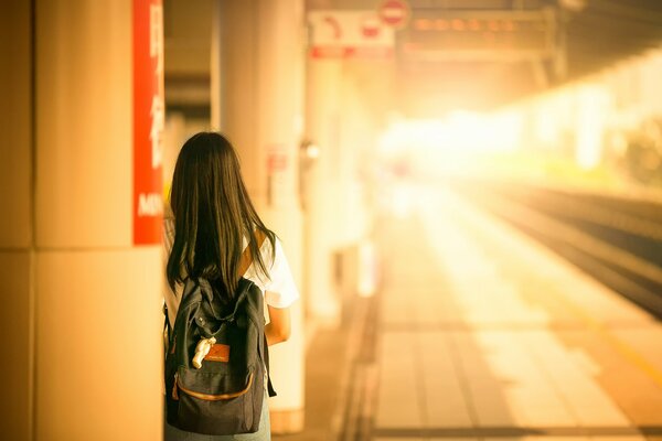 A girl with a backpack is standing at the train station and waiting for the train